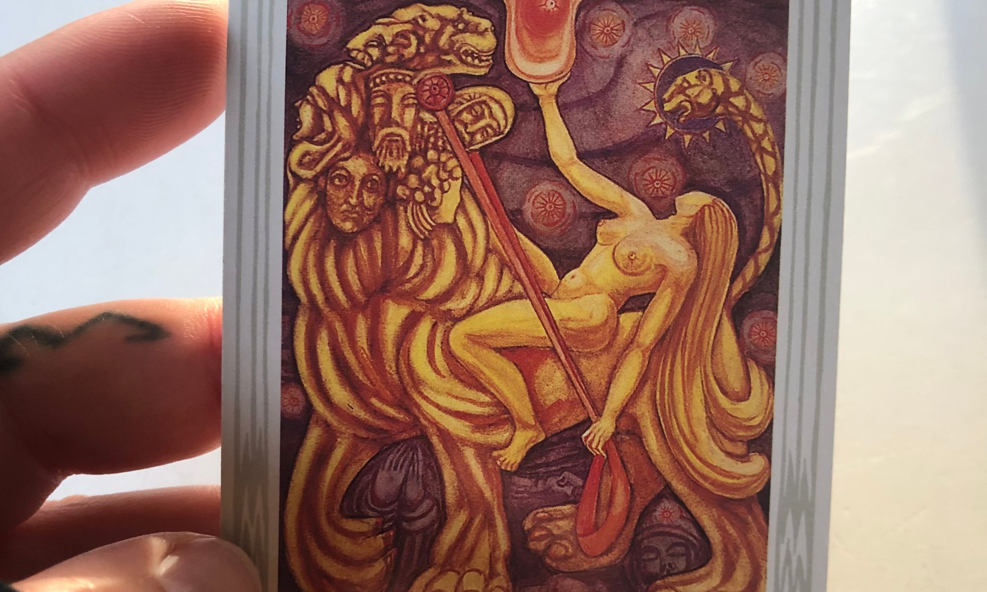 a hand holds the “Lust” or Strength tarot card from the Thoth Tarot Deck